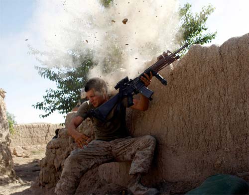 A soldier ducks down behind a mud wall while a bullet kicks its ass